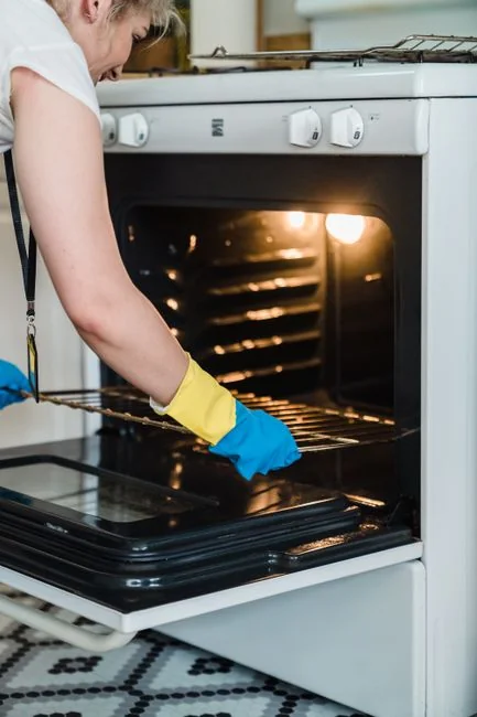 A detailed view of a hand cleaning a stovetop using a spray bottle and cloth.